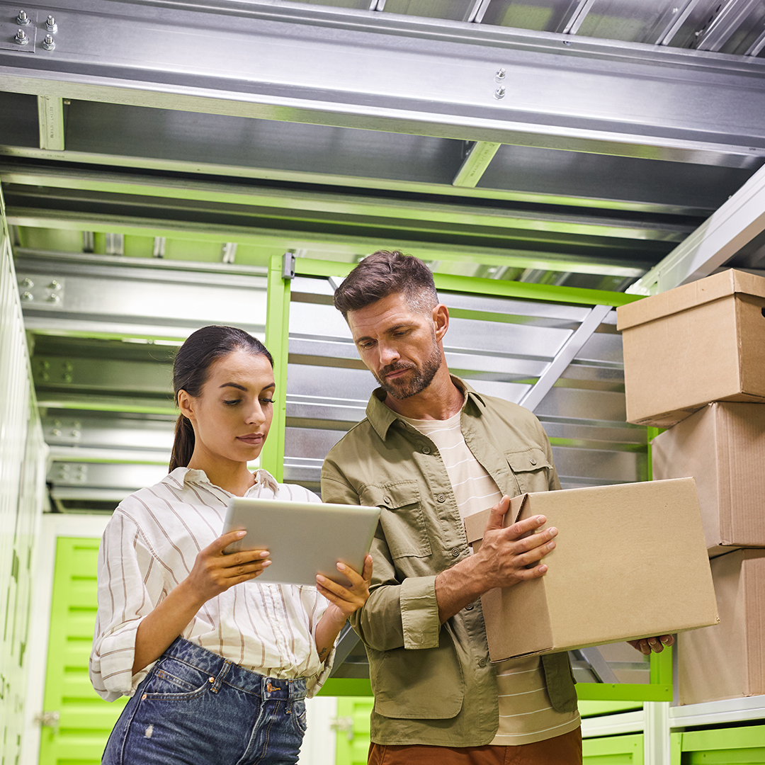 a couple looking at a list together while organizing boxes in a storage unit 