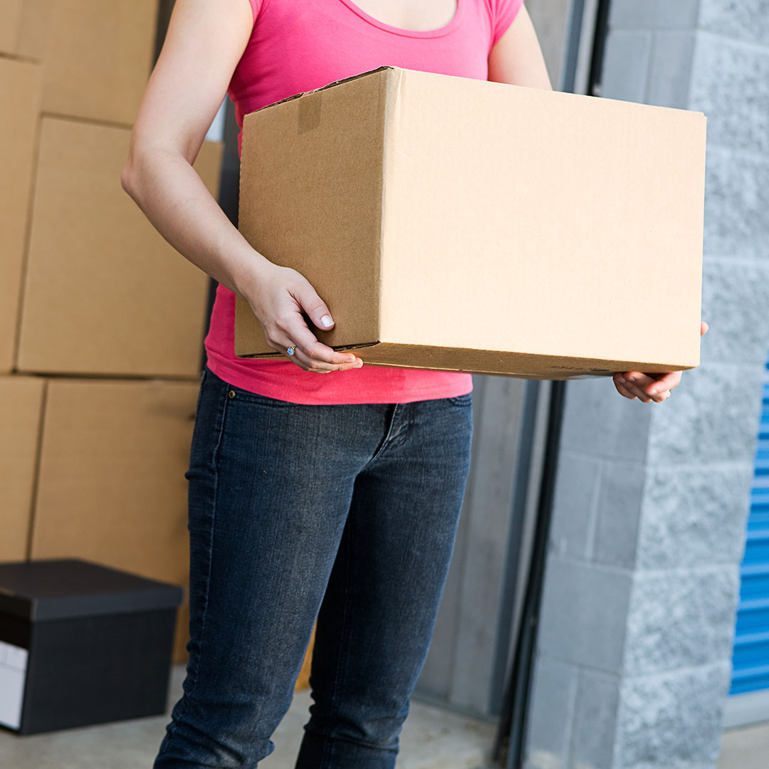woman holding a box next to a storage unit already full of boxes